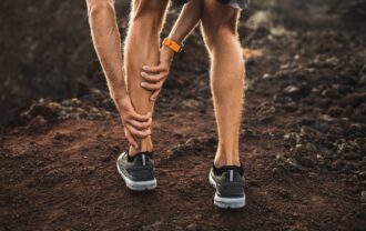 Male runner holding injured calf muscle and suffering with pain. Sprain ligament while running outdoors. View from the back close-up.